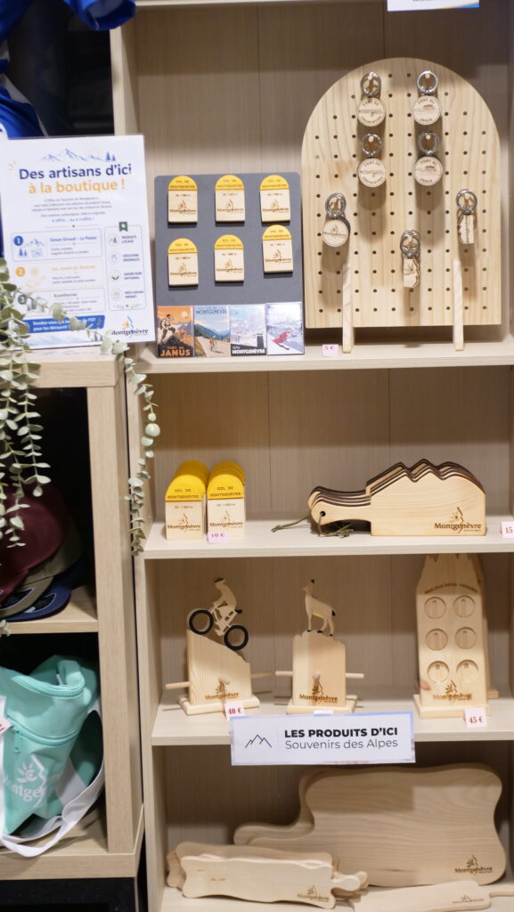 Wooden souvenir display with Montgenèvre keychains on a pegboard and small wooden plaques on shelves.