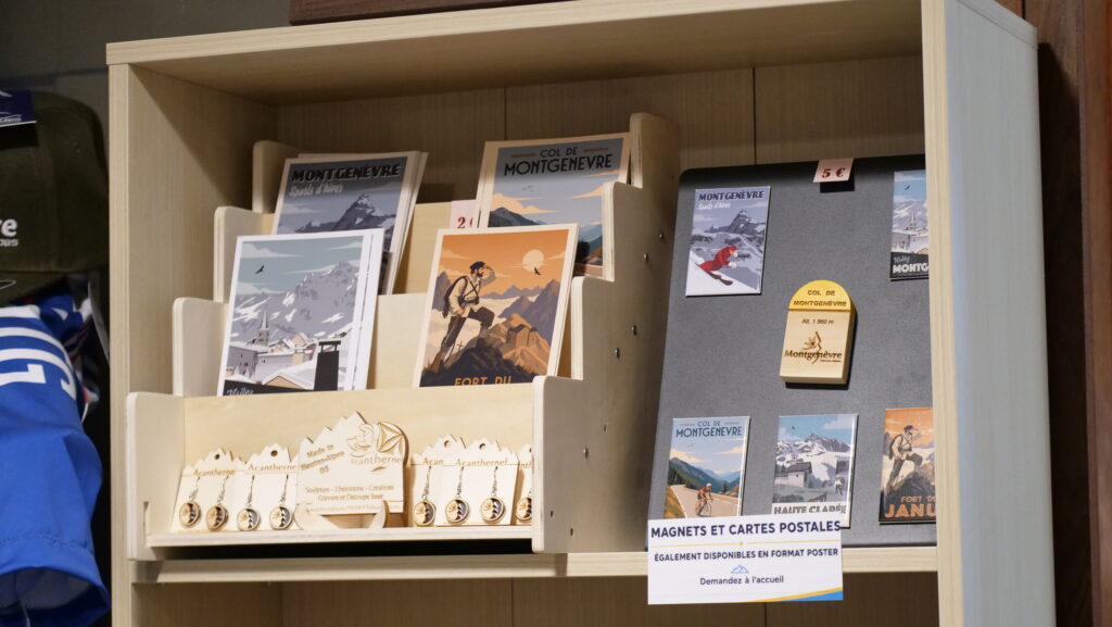 Wooden display shelf filled with vintage travel posters and postcards featuring snow-capped mountains and a climber, with a sign reading 'Magnets et Cartes Postales' on the right panel.