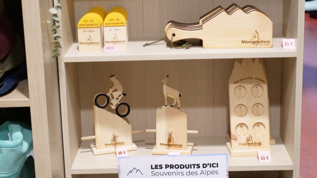 Wooden souvenir shelf with Montgenèvre figures: cyclist, dog, and mountain shapes, with price tags (€40, €45).,