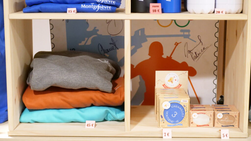 Wooden display shelf with folded clothes on the left and boxed products on the right; several price tags visible (15€, 10€, 20€, 45€, 7€, 5€).